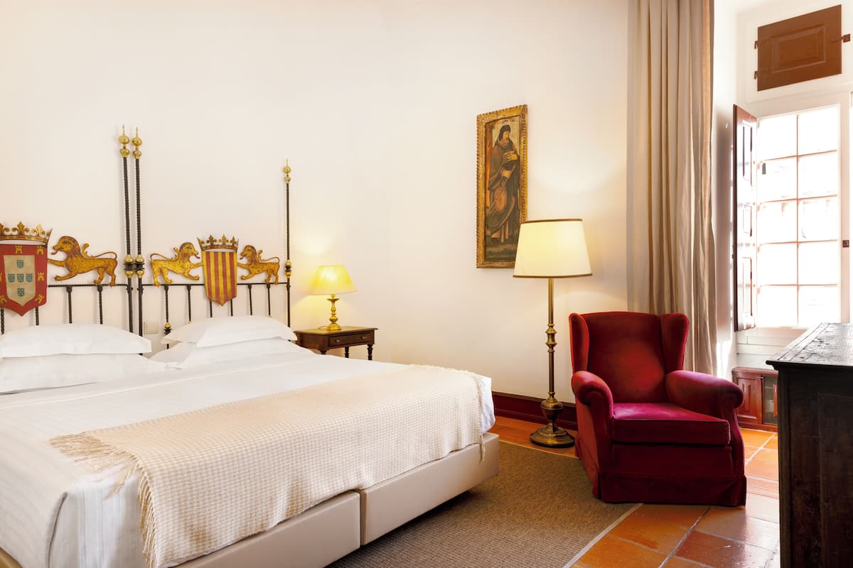 Ein Hotelzimmer mit einem großen Bett, einem roten Sessel, einem Nachttisch mit Lampe und einem Bild an der Wand.
