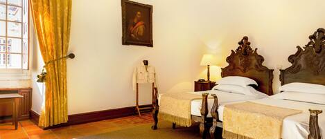 A room with two beds, a wooden headboard, a painting on the wall, and a window with curtains.