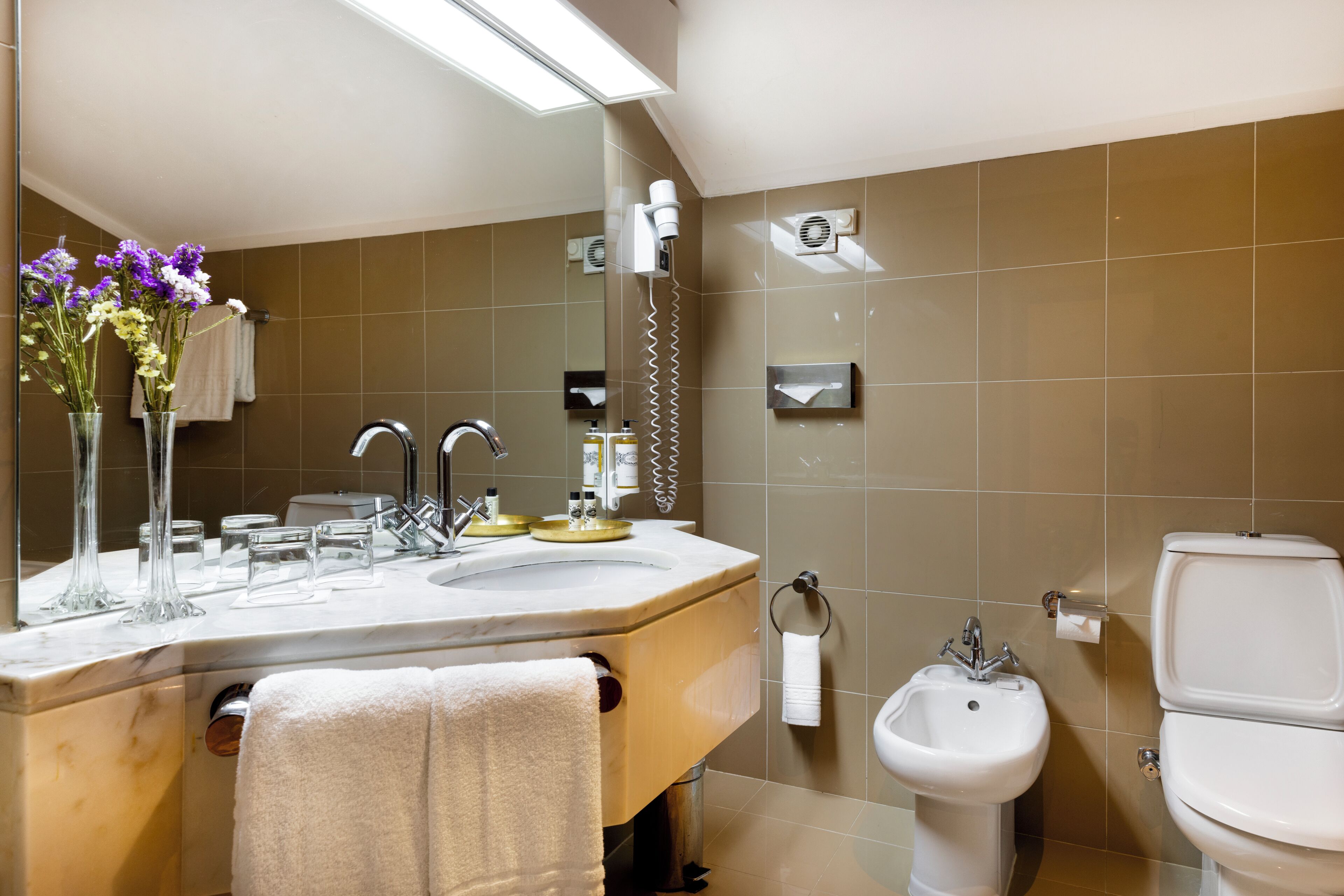 A modern bathroom with a large mirror, a sink with a vanity, a bidet, and a toilet.