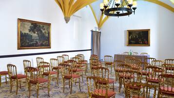 Ein Raum mit Reihen goldener Stühle mit roten Kissen, einer Kristallleuchtre und zwei Bildern an den Wänden.