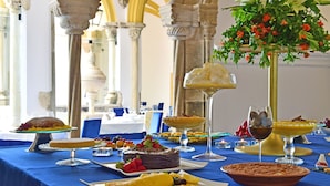 A table set with various desserts and a floral centerpiece, with classical architecture in the background. - Pousada Convento de Evora - Historic Hotel (Évora)