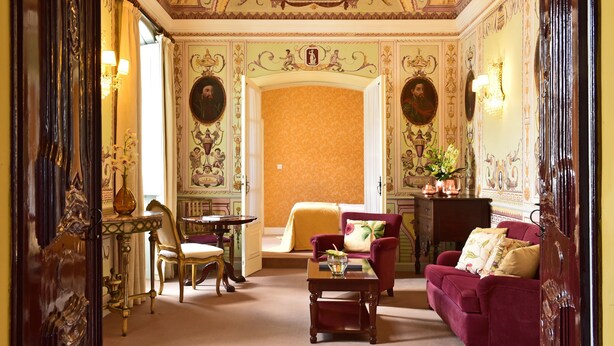 A room with ornate ceiling artwork, a red sofa, a small table, and a chair. - Pousada Convento de Evora - Historic Hotel (Évora)