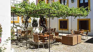 An outdoor patio with wicker furniture, a pergola with vines, and a cobblestone floor. - Pousada Convento de Evora - Historic Hotel (Évora)