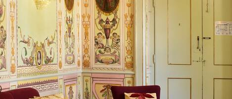 A room with ornate wall decorations, a chandelier, and a door with a sign.