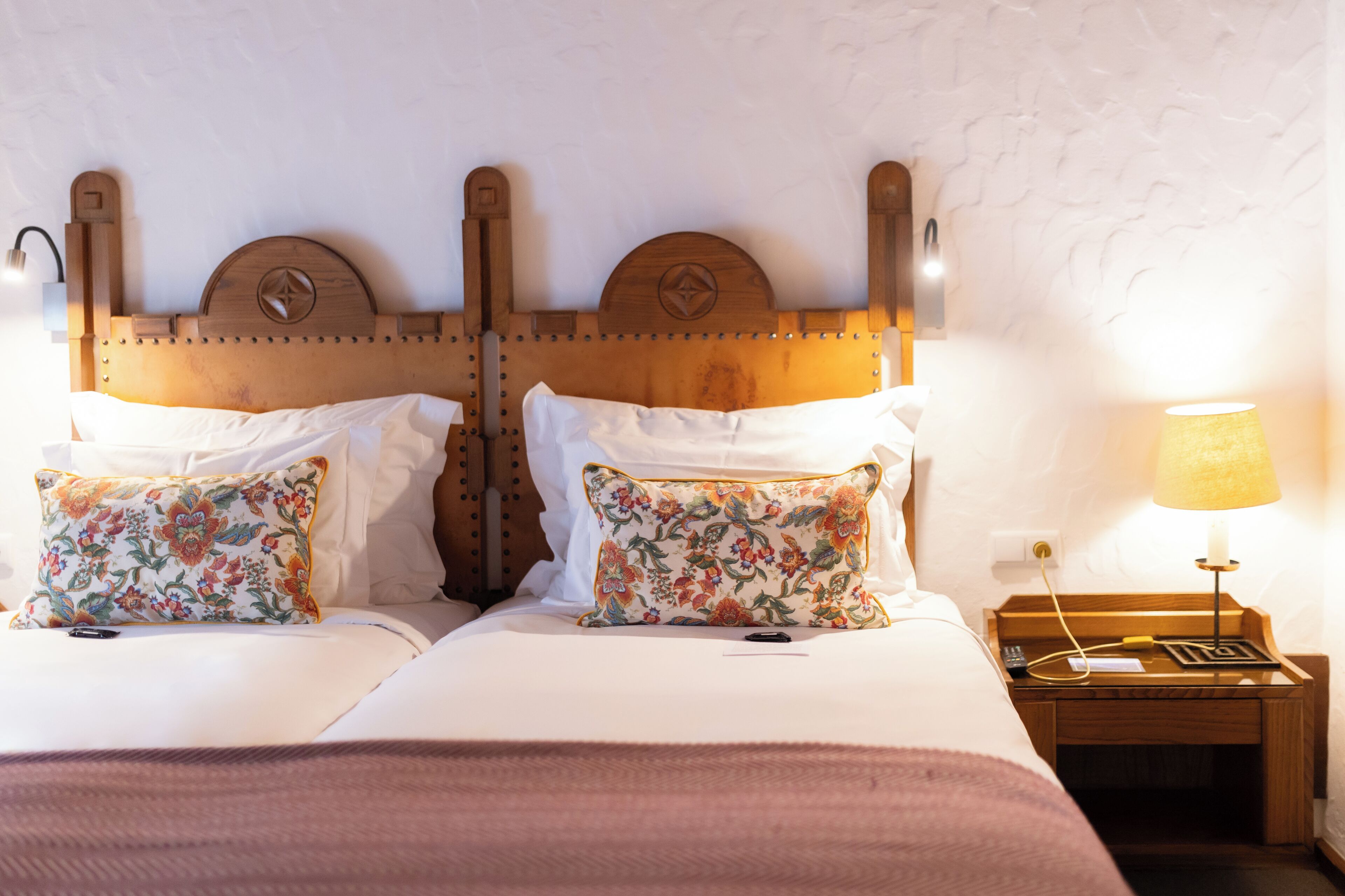 Una cama doble con almohadas estampadas, un cabecero de madera, una mesita de noche con lámpara y una lámpara de pared.