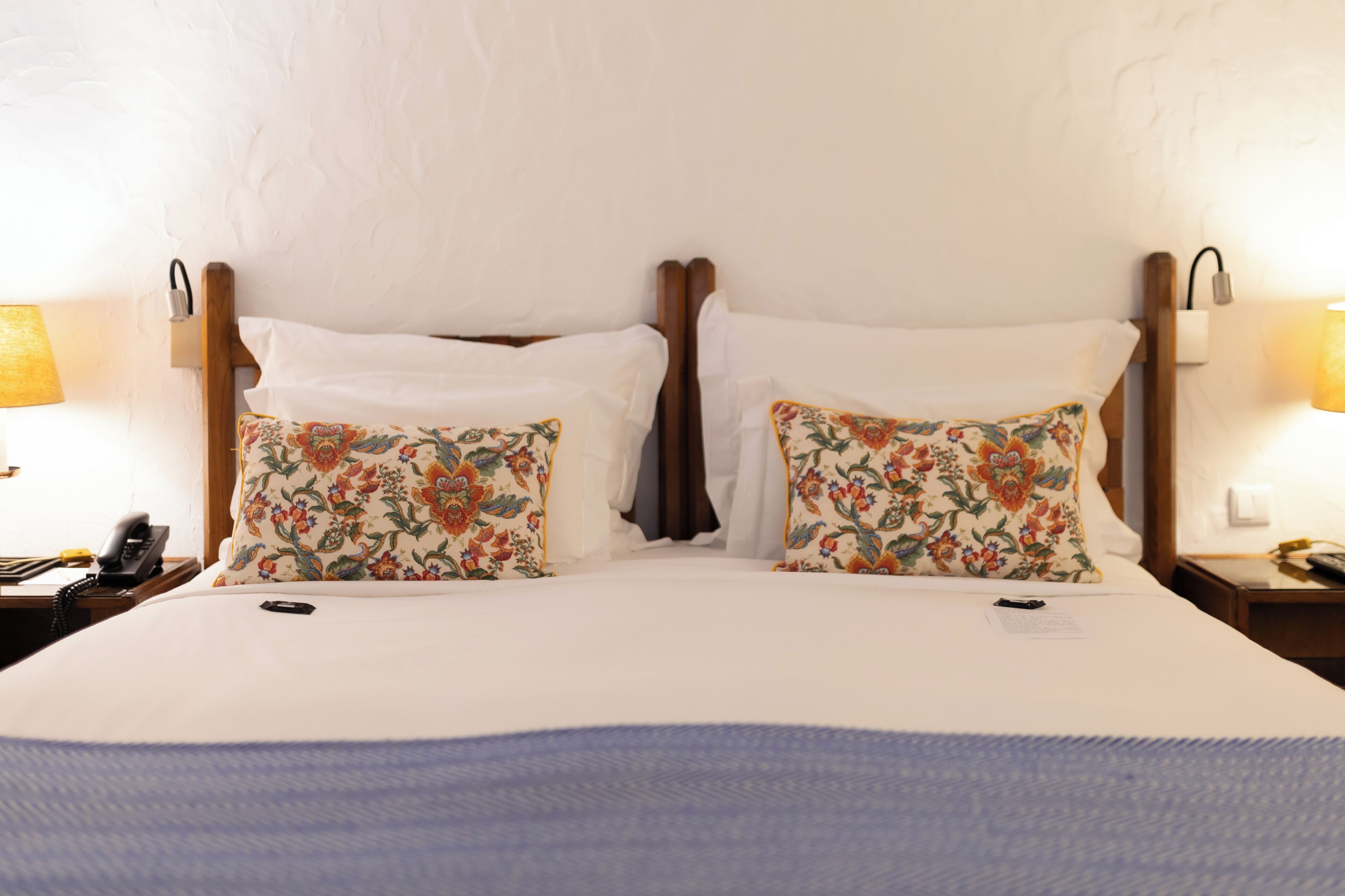 Un lit double avec des oreillers à motifs floraux, un téléphone sur la table de chevet et une lampe de chaque côté.