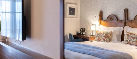 A hotel room with a large bed, a desk with a lamp, a television, and a framed picture on the wall.