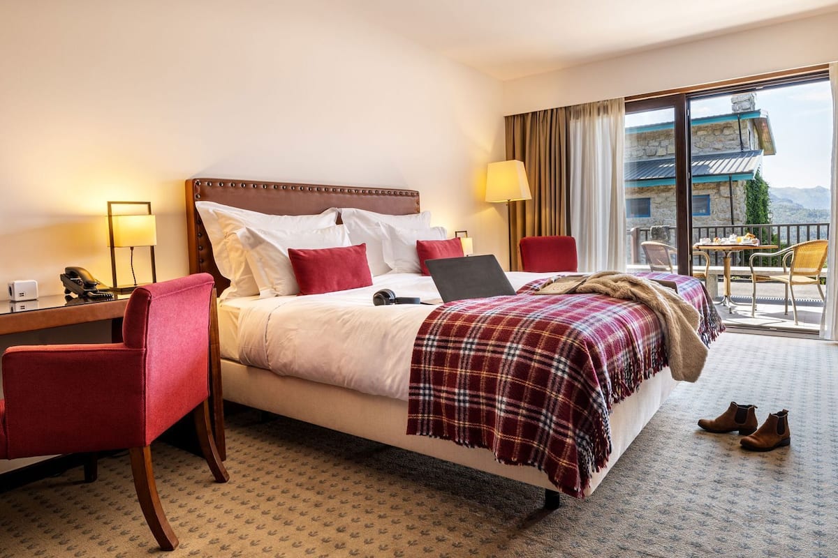 Een hotelkamer met een bed, een bureau, een stoel, een laptop en uitzicht op het omliggende landschap.