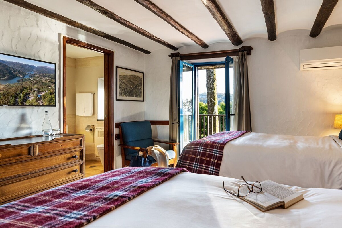 Hotelkamer met twee bedden, een houten dressoir, een stoel, een televisie en een balkon met uitzicht.