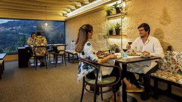 Un comedor con una mesa dispuesta para dos, vistas al exterior y una repisa con plantas.