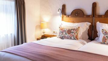 Une chambre d’hôtel avec un grand lit, une tête de lit en bois, une table de chevet avec une lampe et une fenêtre avec des rideaux.