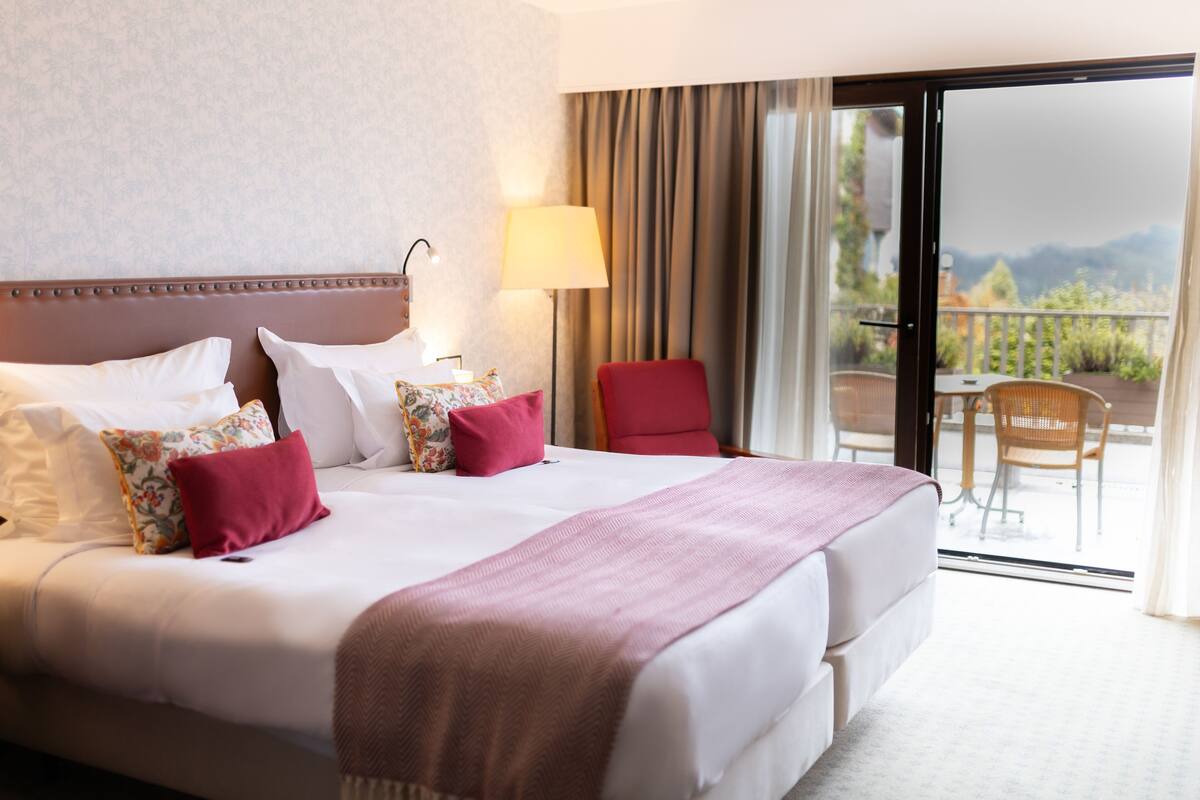 Een hotelkamer met een groot bed, een rode stoel, een tafel en uitzicht op de omgeving.