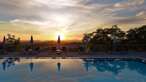 A poolside area with lounge chairs and umbrellas, reflecting the sunset and mountains in the background.