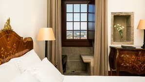 A hotel room with a bed, a desk, a lamp, a window with a view, and a small staircase.