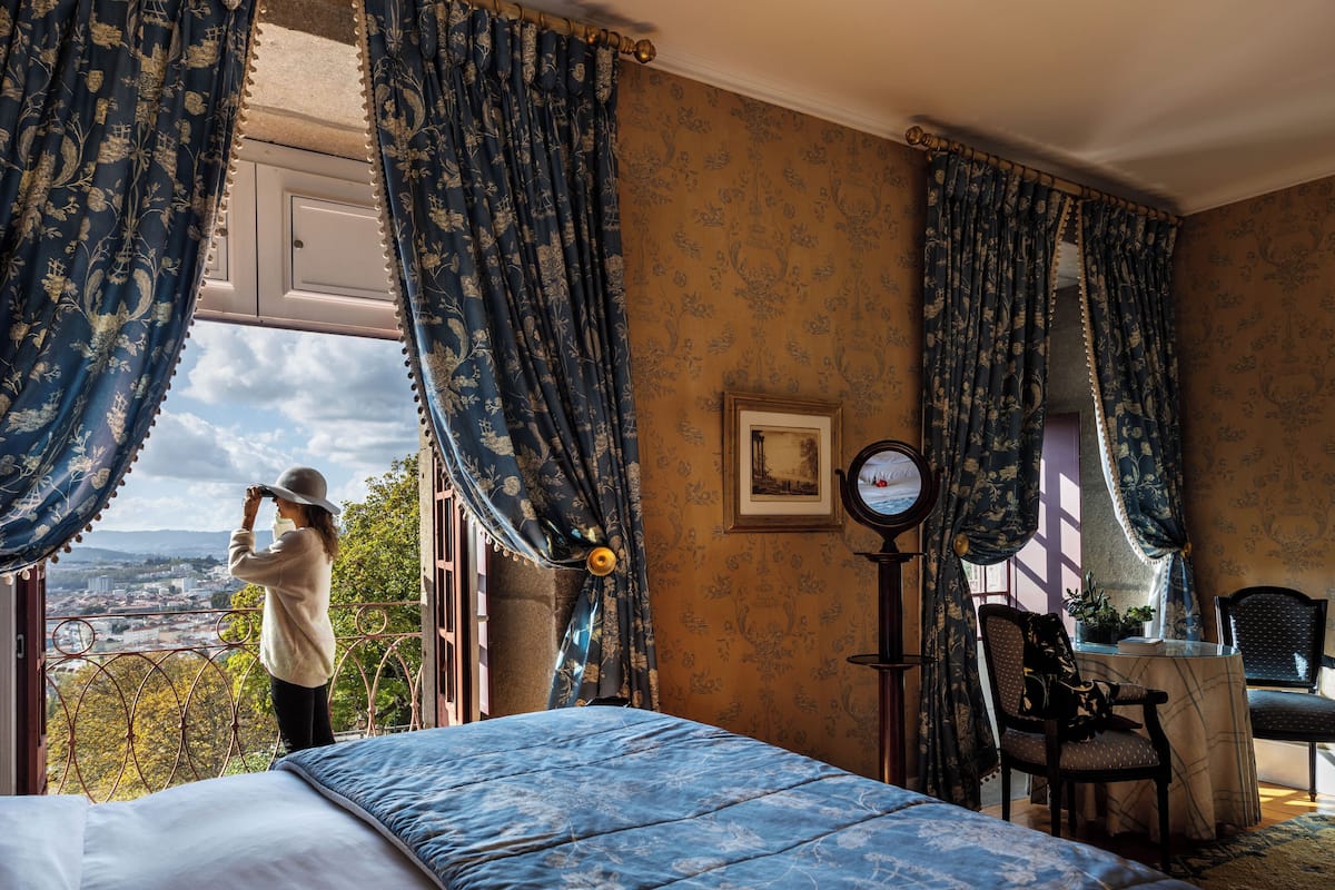 Une chambre à coucher avec un grand lit, une chaise, une petite table et une fenêtre avec des rideaux.