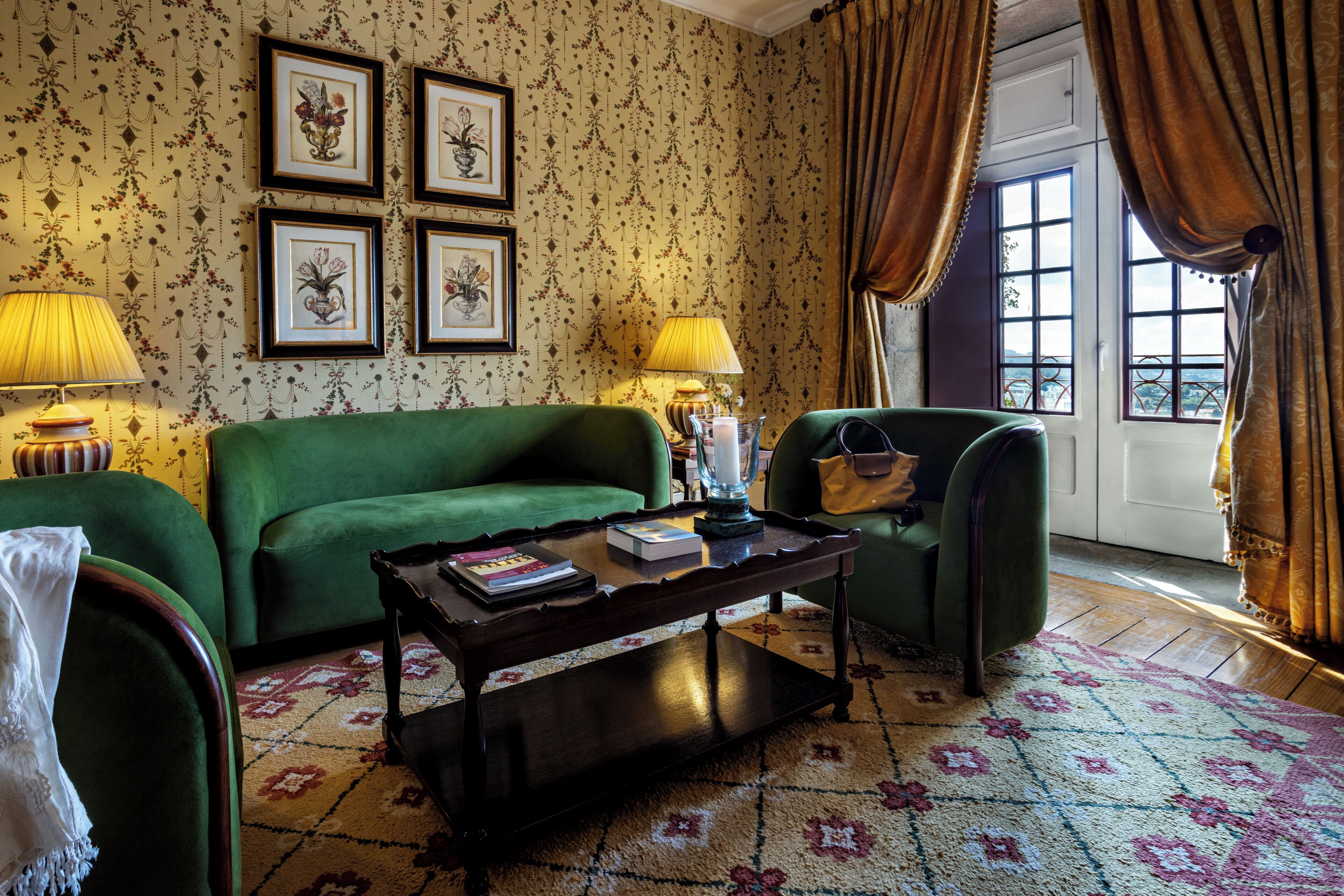 Una habitación con un sofá verde, una mesa de centro de madera con libros, dos lámparas y una alfombra estampada.
