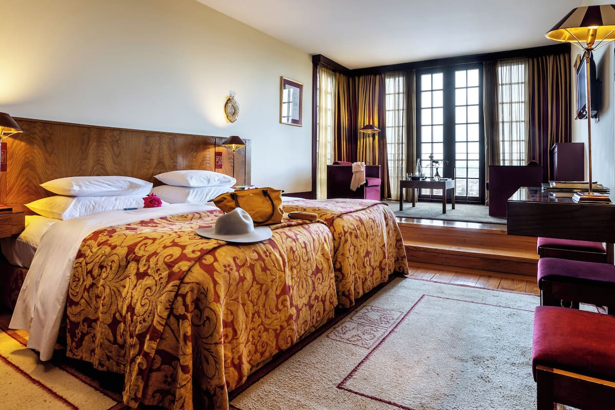 Une chambre d’hôtel avec un grand lit, un bureau, une chaise et une vue sur la ville par les fenêtres.