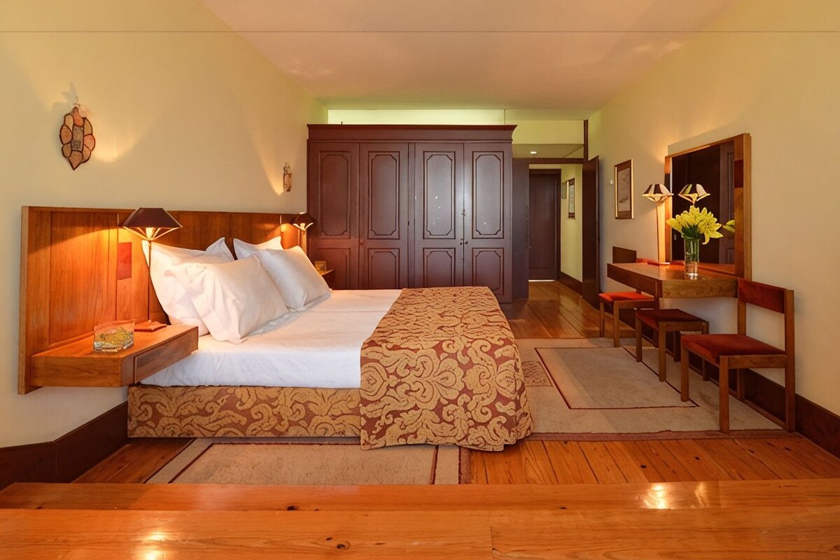 A hotel room with a bed, bedside tables, a wardrobe, a mirror, and a seating area with chairs.