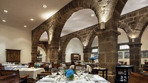 Un restaurante con arcos de piedra, mesas dispuestas para comer y una araña.