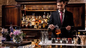 A bar with a bartender preparing a drink, various bottles and jars of ingredients, and a wooden counter.