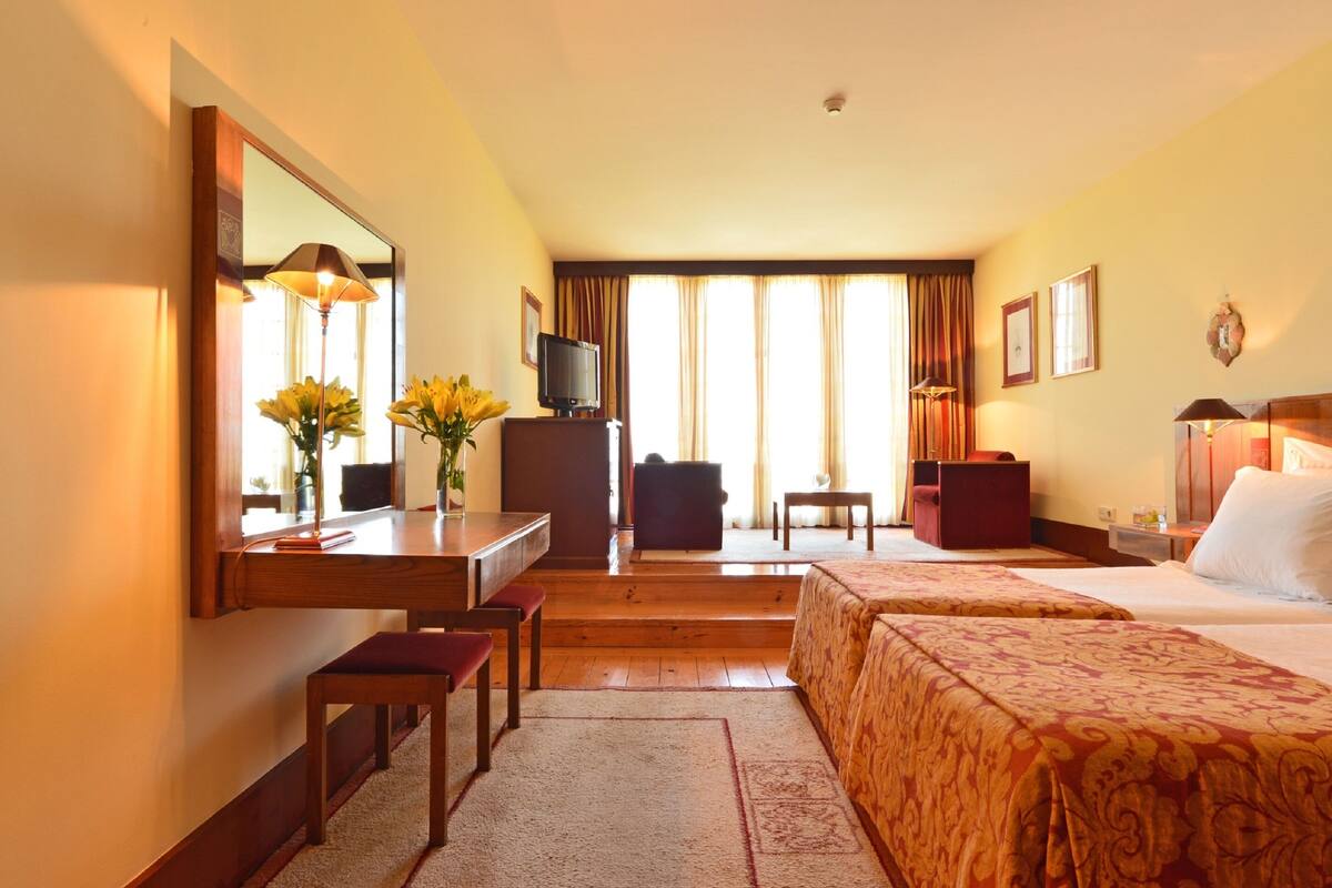 Une chambre d’hôtel avec deux lits, un bureau avec une chaise, une télévision et un grand miroir.