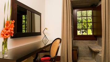 A bathroom with a wooden vanity, a mirror, a chair, a vase with flowers, and a window with curtains.