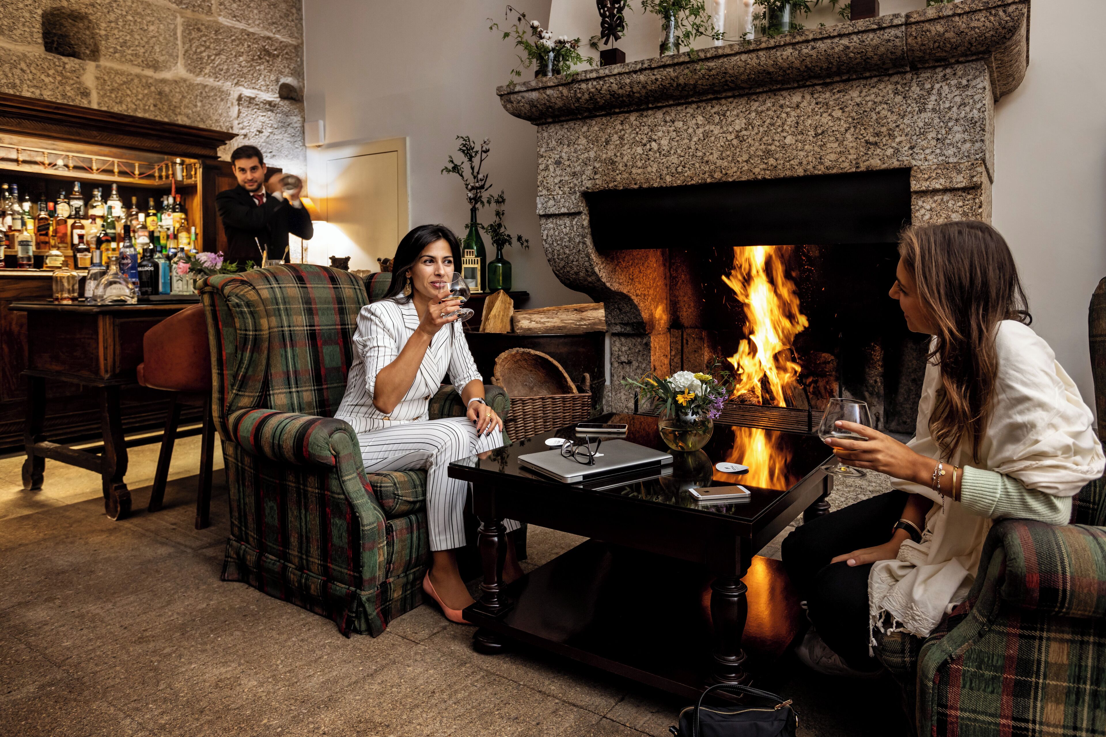 A cozy lounge area with a fireplace, comfortable seating, and a bar with various bottles.