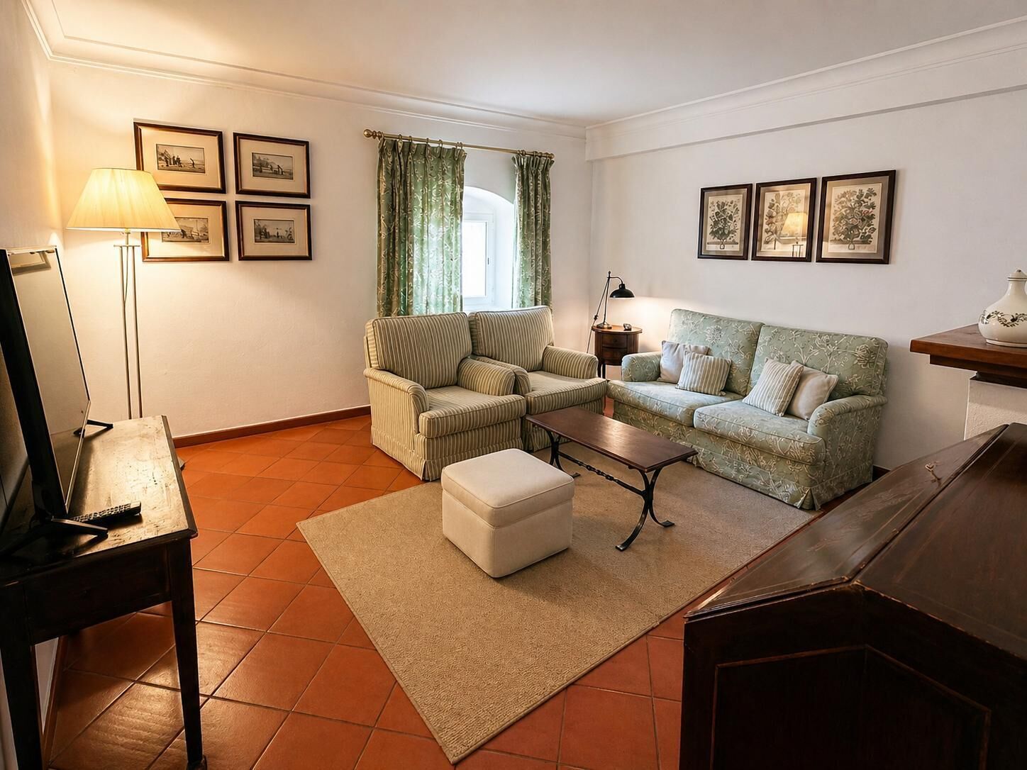 A living room with a sofa, armchair, ottoman, coffee table, lamp, and framed pictures on the wall.