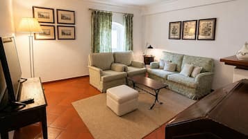 A living room with a sofa, armchair, ottoman, coffee table, lamp, and framed pictures on the wall.