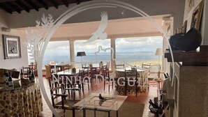 A dining area with a view of the mountains, a glass table, and chairs. There are wine bottles on a shelf and a framed picture on the wall. - Pousada do Marvão - Charming Hotel (Marvao)