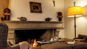 A cozy living room with a fireplace, a comfortable sofa, a table with a glass of wine, and a lamp. - Pousada do Marvão - Charming Hotel (Marvao)