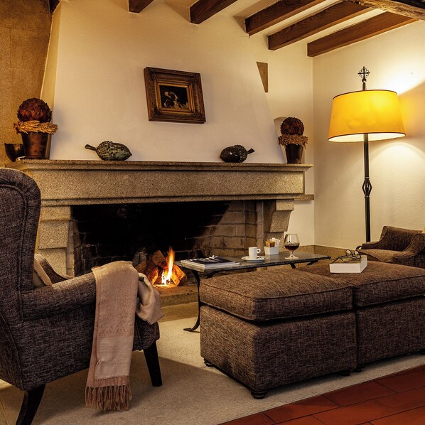 A cozy living room with a fireplace, a comfortable sofa, a table with a glass of wine, and a lamp.