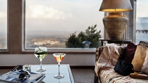 A room with a view of a cityscape, a table with two glasses of beverages, a lamp, and a sofa with cushions. - Pousada do Marvão - Charming Hotel (Marvao)