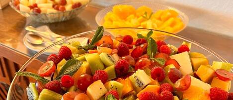 A fruit salad with various fruits and mint leaves on a glass serving dish.