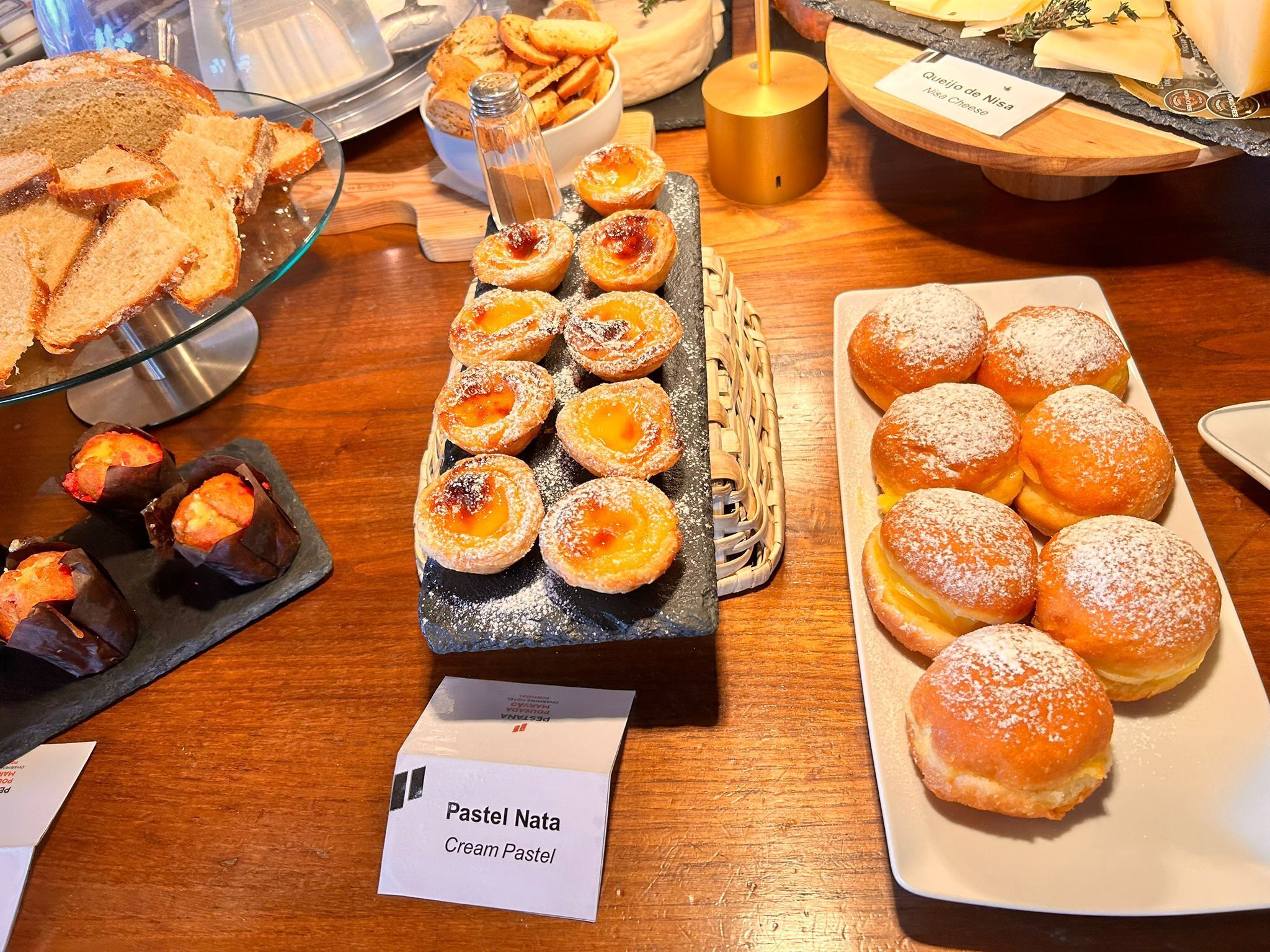 A variety of pastries and bread on display, including pastel nata and cream pastel.