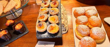 A variety of pastries and bread on display, including pastel nata and cream pastel.
