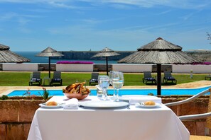 Mesa lista para comer con vista al océano y a una piscina.