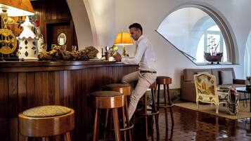A man sitting at a bar with stools, a lamp, and a ship model in the background.