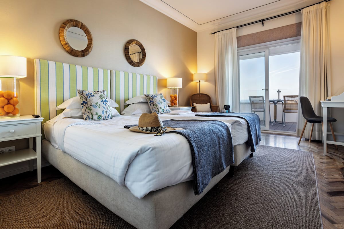 Ein Hotelzimmer mit einem großen Bett, zwei Nachttischen, einem Schreibtisch und einem Balkon mit Sitzgelegenheiten.