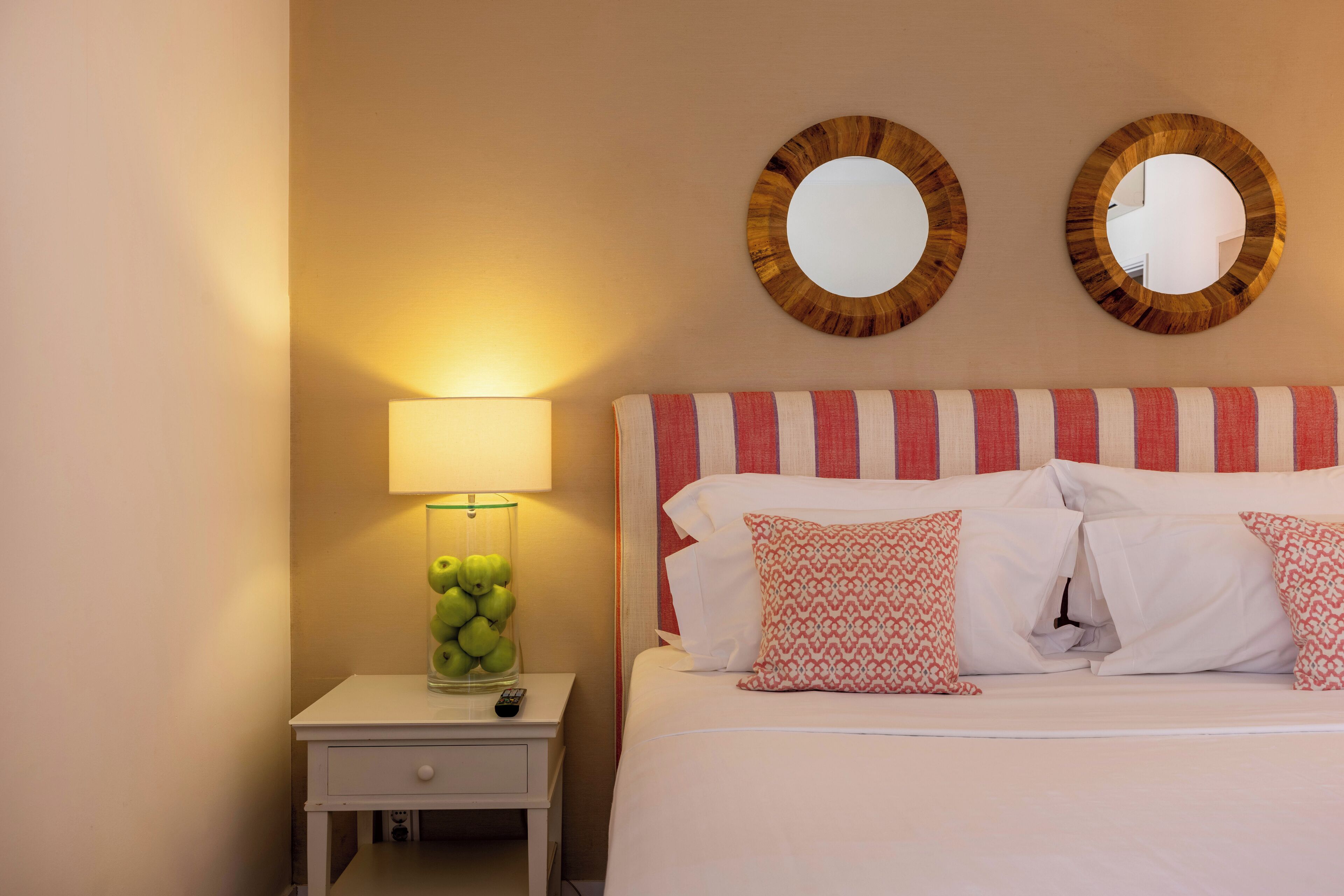 A hotel room with a bed, a nightstand with a lamp and a vase of apples, and two wall mirrors.