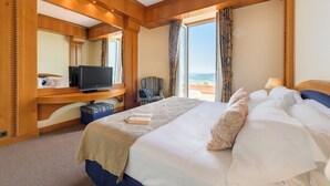 Une chambre d’hôtel avec un grand lit, un téléviseur posé sur un meuble en bois, une chaise et une vue sur l’extérieur grâce à de grandes fenêtres.