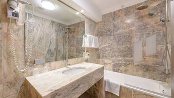 A bathroom with a marble sink, a large mirror, a handheld showerhead, and a bathtub.