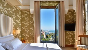 Une chambre d’hôtel avec un lit, une chaise, une télévision et un balcon donnant sur un paysage urbain.