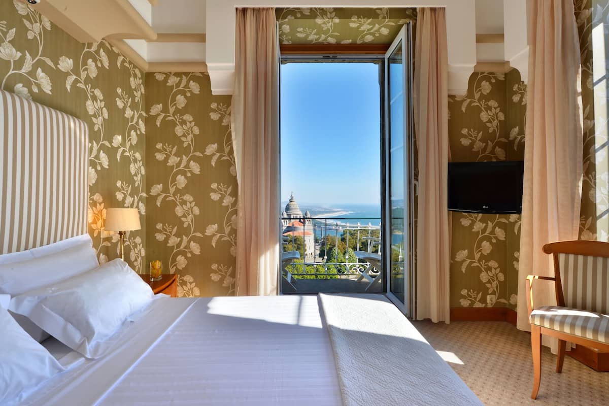 Habitació d'hotel amb llit, cadira, televisió i balcó amb vista a la ciutat.