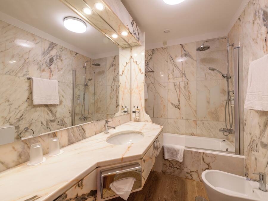 A modern bathroom with a marble sink, a large mirror, a glass-enclosed shower, and a separate bathtub.