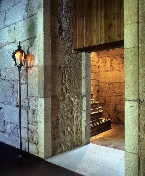 A stone-walled corridor with a wooden door and a lit wall-mounted lamp. - Lam Hotel Convento do Desagravo (Oliveira do Hospital)