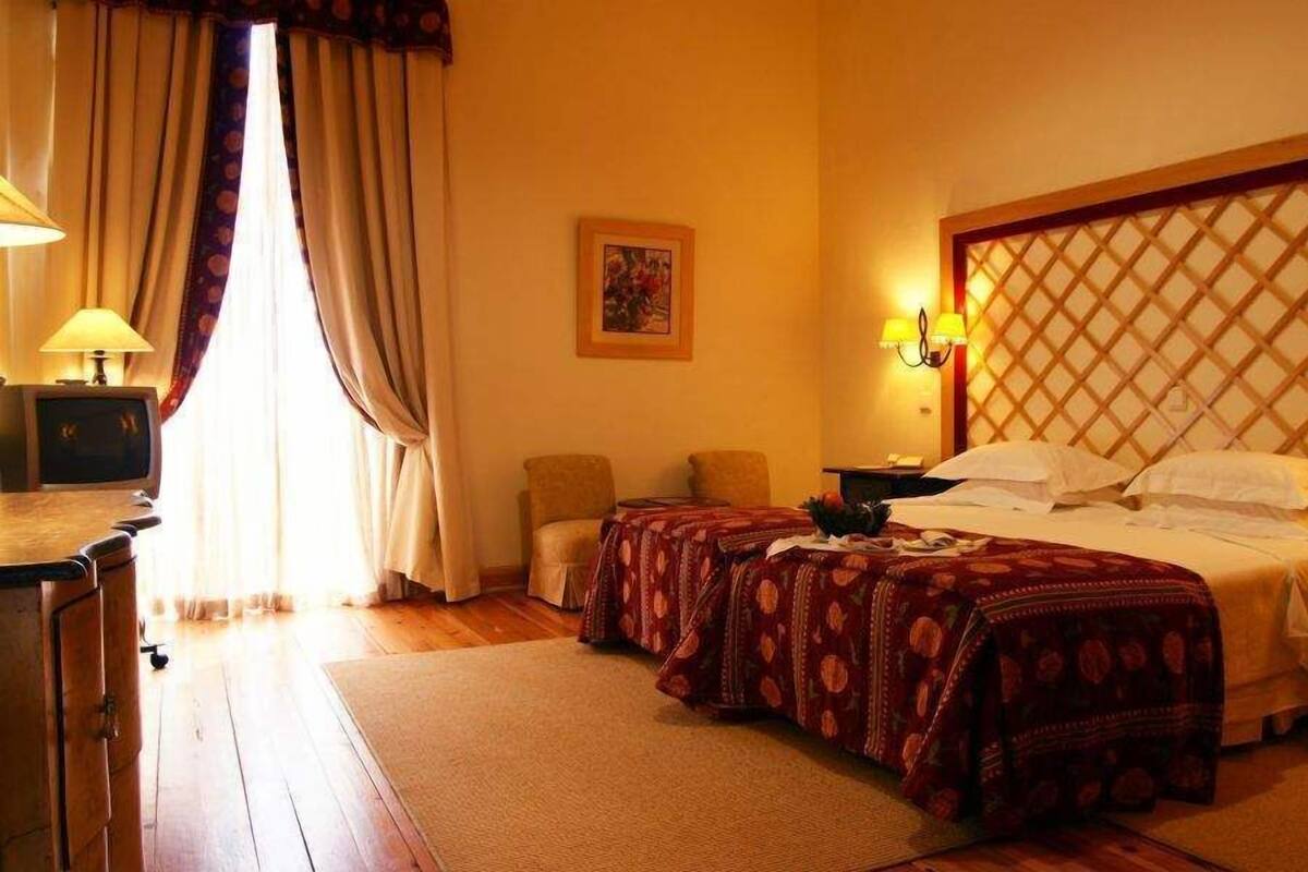Habitación de hotel con cama doble, dos mesitas de noche, un escritorio con lámpara, una silla y un ventanal con cortinas.