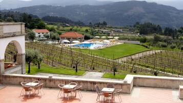 A terrace with outdoor seating and a view of a swimming pool, vineyards, and distant mountains.