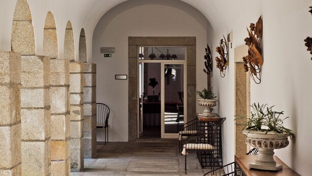 An interior corridor with stone arches, a seating area with metal chairs, and a potted plant on a wooden table. - Lam Hotel Convento do Desagravo (Oliveira do Hospital)
