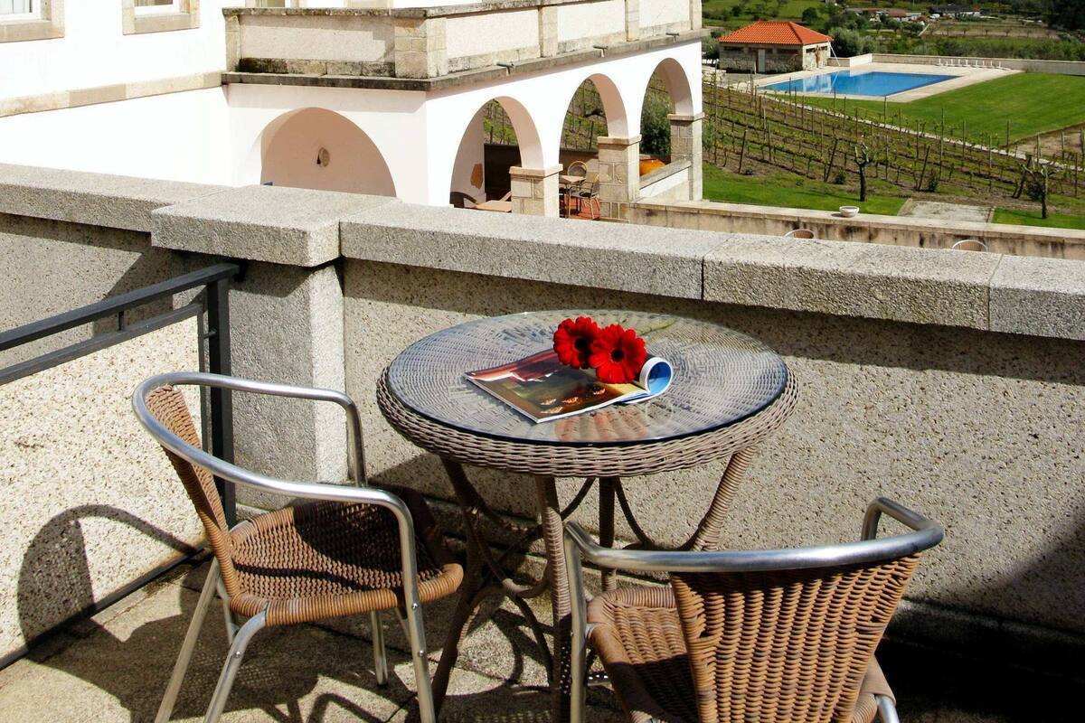 Una terraza con sillas de mimbre y una mesa, con vistas a una piscina y un paisaje montañoso.